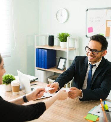 Happy professional man smiling and exchanching business cards with a female colleague. Caucasian woman giving her number and contact information to a latin man in a suit